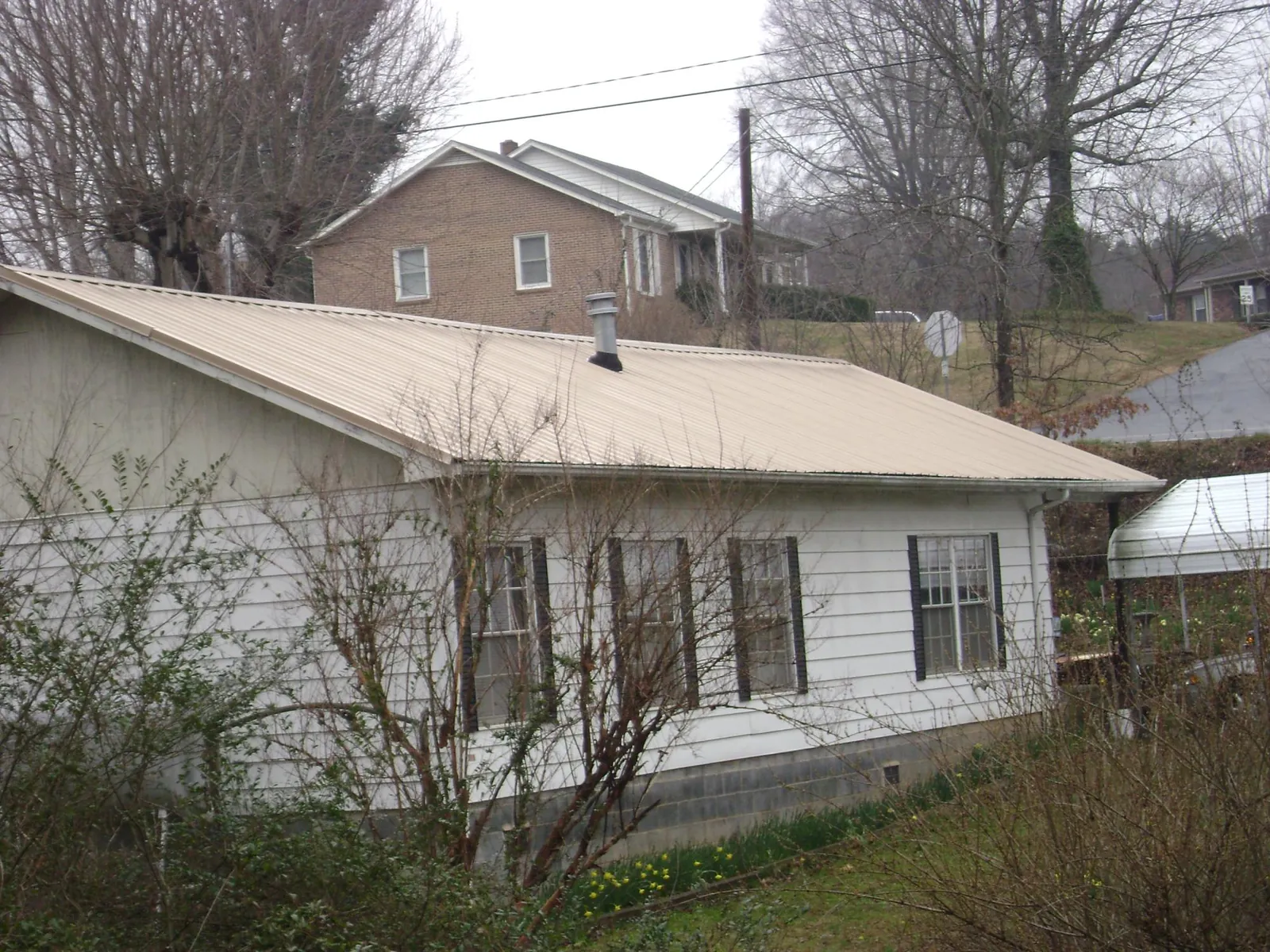Tan metal roof on a white sided house set into a hillside — Commercial Roofing by Roofing Brothers in Boca Raton